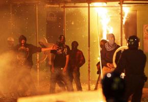 Police look on as rioters pass a blazing building in North London